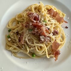 a white plate topped with pasta covered in bacon and parmesan sprinkles