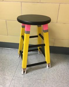 a black and yellow stool sitting in front of a brick wall with pink and yellow tape on it