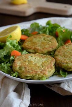 two crab cakes on a plate with lettuce and carrots next to lemon wedges