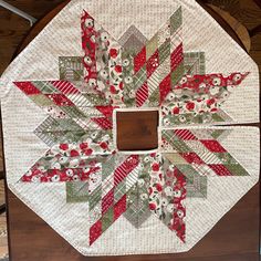 a quilted table topper with red, green and white flowers in the center