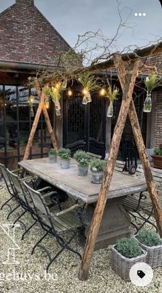 an outdoor dining area with potted plants on the table and lights hanging from the roof