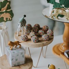 there are many toy animals on the cake plate and in the background is an elephant, zebra, giraffe