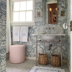 a bathroom with blue and white wallpaper has a sink, mirror, and stool