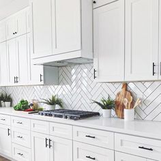 a kitchen with white cabinets and wooden cutting board on the stove top, surrounded by potted plants