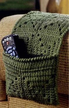 a remote control in a green crocheted basket on a couch with a pillow