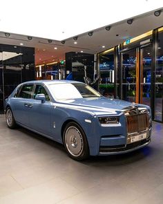 a blue rolls royce parked in front of a glass building with an open door and entrance