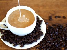 a cup of coffee sitting on top of a white saucer filled with coffee beans