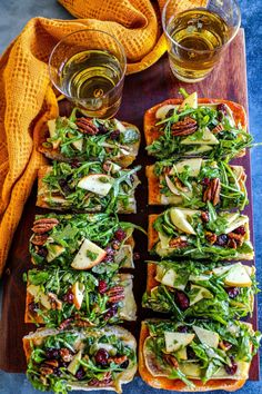 several slices of bread with salad and apples on them next to two glasses of beer