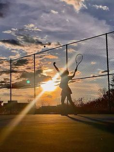 a person holding a tennis racquet on top of a tennis court at sunset