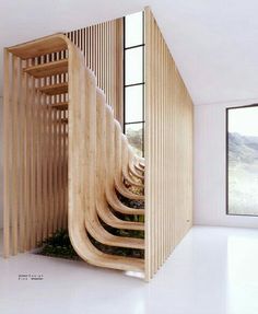 a spiral staircase made out of wooden slats in a room with large windows and white flooring