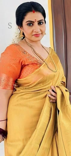 a woman in an orange and yellow sari posing for the camera with her hands on her hips