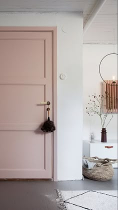 a pink door in a white room next to a basket and vase with flowers on it