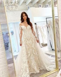 a woman standing in front of a mirror wearing a wedding dress with long sleeves and an open back