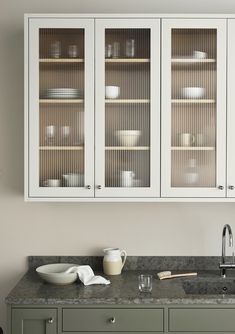 a kitchen with white cabinets and gray counter tops, dishes on the shelves in front of them