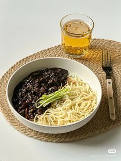 a white bowl filled with noodles and vegetables next to a glass of beer on a place mat