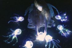 a woman is surrounded by jellyfish in the dark with glowing lights on her body