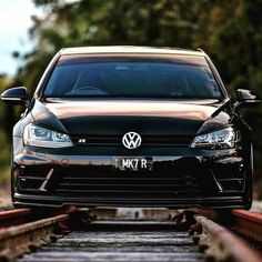 the front end of a black volkswagen golf gtr on a track with trees in the background