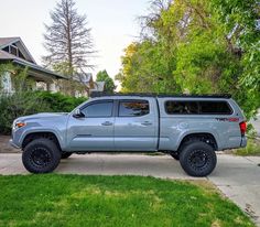 a gray truck parked on the side of a road next to a tree and house