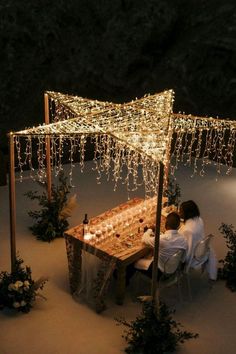 two people are sitting at a table under a lit up gazebo with candles on it