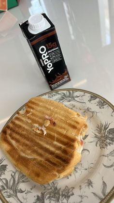 a sandwich on a plate next to a carton of oatmeal milk