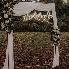 a white wedding arch decorated with flowers and greenery for an outdoor ceremony in the fall