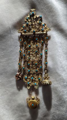 an ornate gold necklace with turquoise beads and bells hanging from it's side on a white cloth