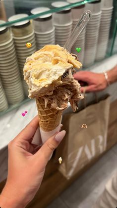 someone is holding an ice cream cone with some sort of topping on it in front of stacks of plates