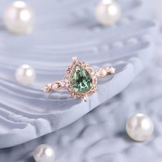 a ring with a green stone surrounded by pearles on a blue cloth and white pearls