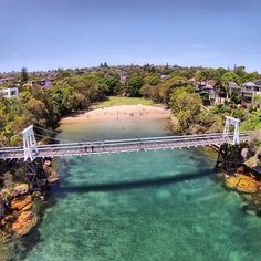 an aerial view of a bridge over clear blue water with houses in the background and people walking on it