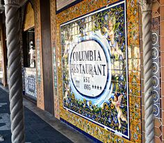 a restaurant sign on the side of a building next to a sidewalk with columns and pillars