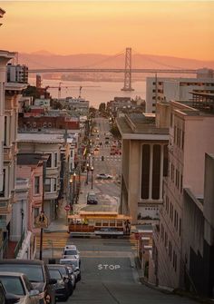 a city street with cars parked on both sides and a bridge over the water in the background