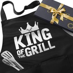 a black apron with the words king of the grill on it next to a gift box