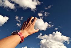 a hand reaching up into the sky to catch a frisbee with clouds in the background