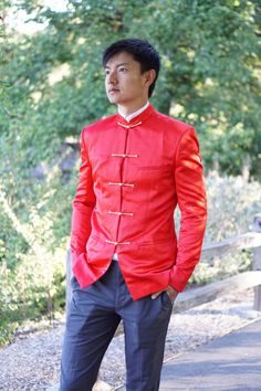 a man in a red jacket and black pants standing on a path with trees behind him