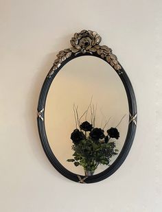 a mirror hanging on the wall with flowers in front of it and a vase filled with black roses