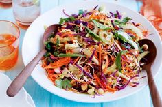 a salad with carrots, cabbage and sprouts in a white bowl on a blue table