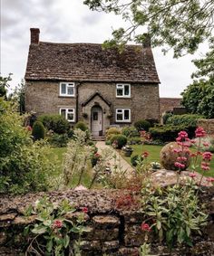 a stone house surrounded by flowers and greenery