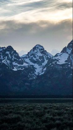 the mountains are covered in snow as the sun is low to the ground and dark clouds can be seen above them