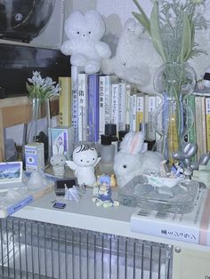 there are many stuffed animals sitting on the table next to books and vases with flowers in them