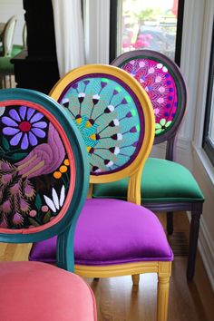 four colorful chairs sitting on top of a hard wood floor next to a window in a room