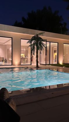 an empty swimming pool at night in front of a house with large glass doors and windows