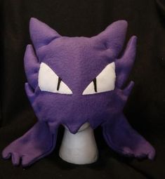 a purple stuffed animal with white eyes and big claws on it's head, sitting in front of a black background