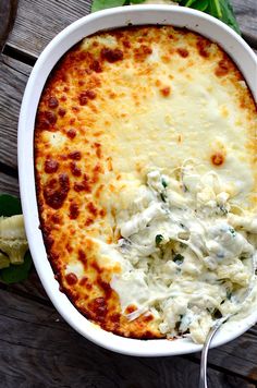 a casserole dish with cheese and spinach in it on a wooden table