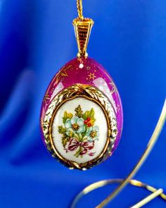 a purple and white glass ornament hanging from a gold plated chain on a blue background