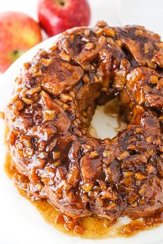 a bundt cake covered in caramel and nuts on a plate next to apples