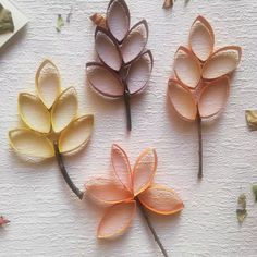 three paper flowers are arranged on a white surface, with leaves scattered around the petals