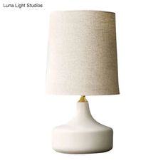 a white lamp sitting on top of a table next to a beige shade light bulb