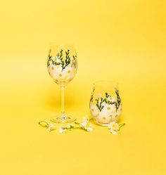 two wine glasses sitting next to each other on a yellow surface with flowers painted on them