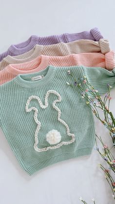 four knitted sweaters sitting on top of each other next to some dried flowers