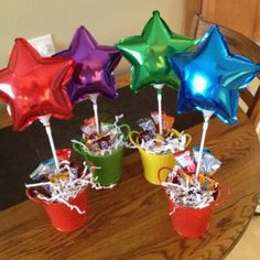 four colorful star shaped balloons in buckets on a table with candy and candies